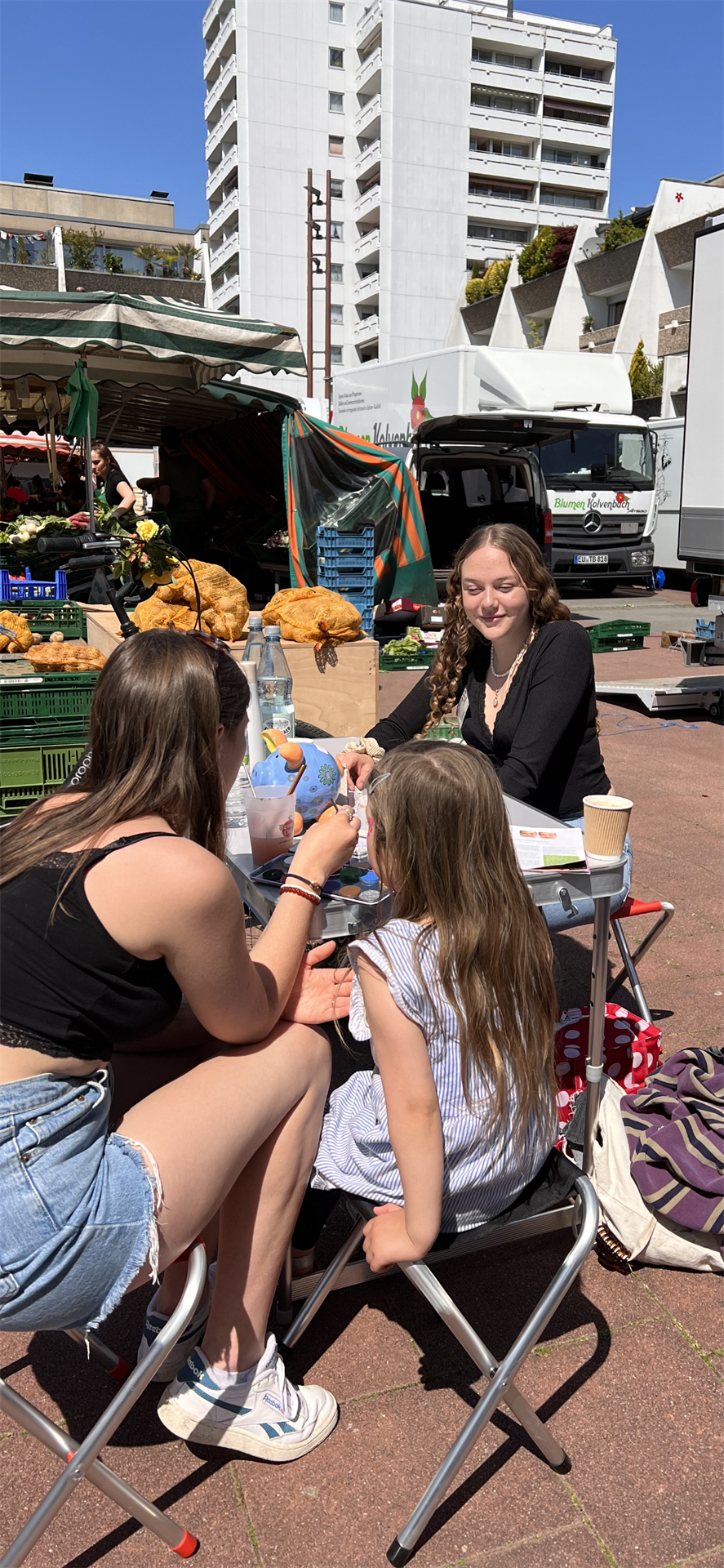 Das Bild zeigt zwei Erwachsene und ein Kind, das geschminkt wird.
